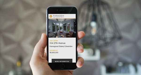 A hand holding a mobile device displaying a mini-site made with the DASH Marketing real-estate web app.